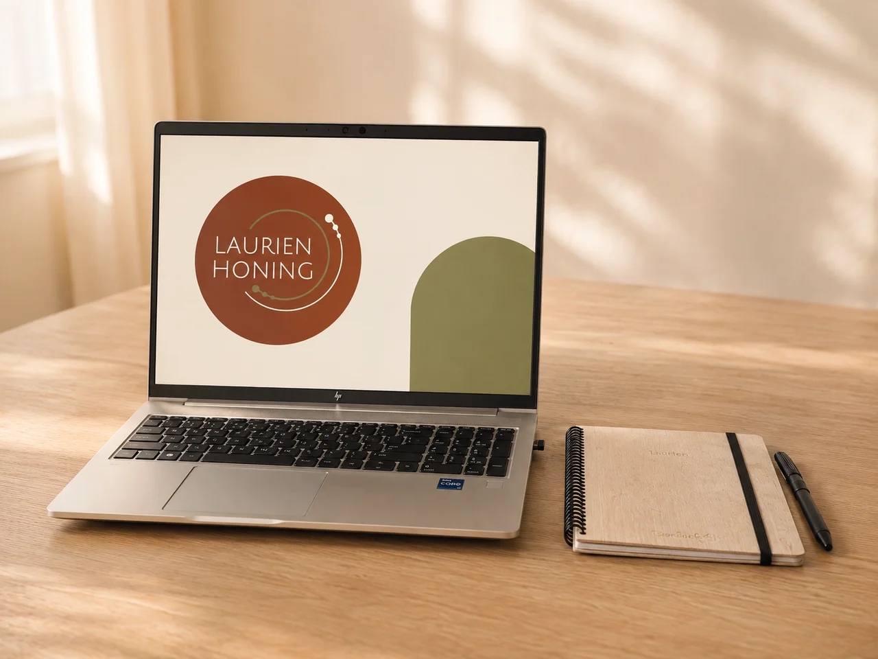 Laptop met Laurien Honing-logo op een rustige werkplek met een notitieboek